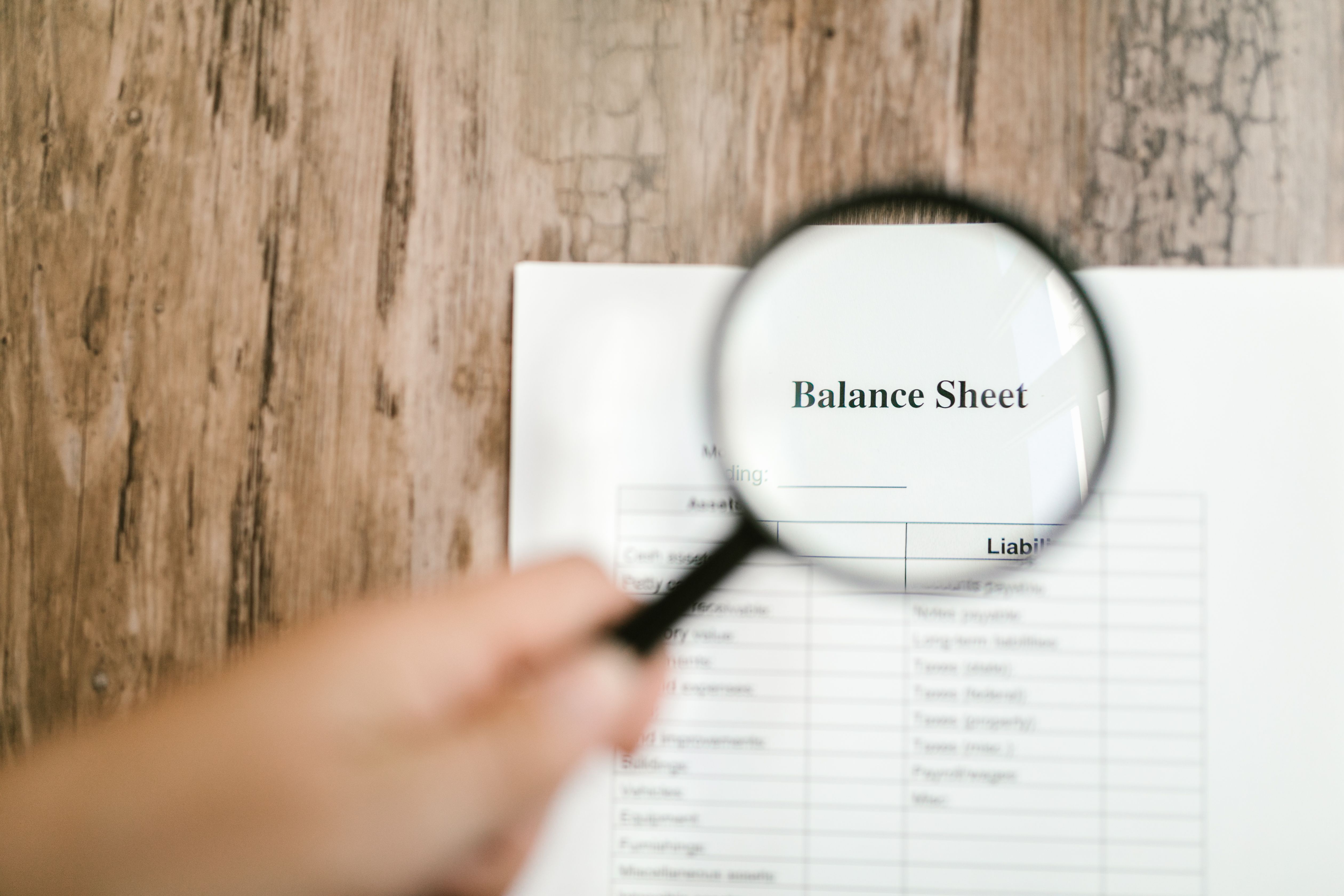 Close-up of a balance sheet document on a wooden surface with a magnifying glass