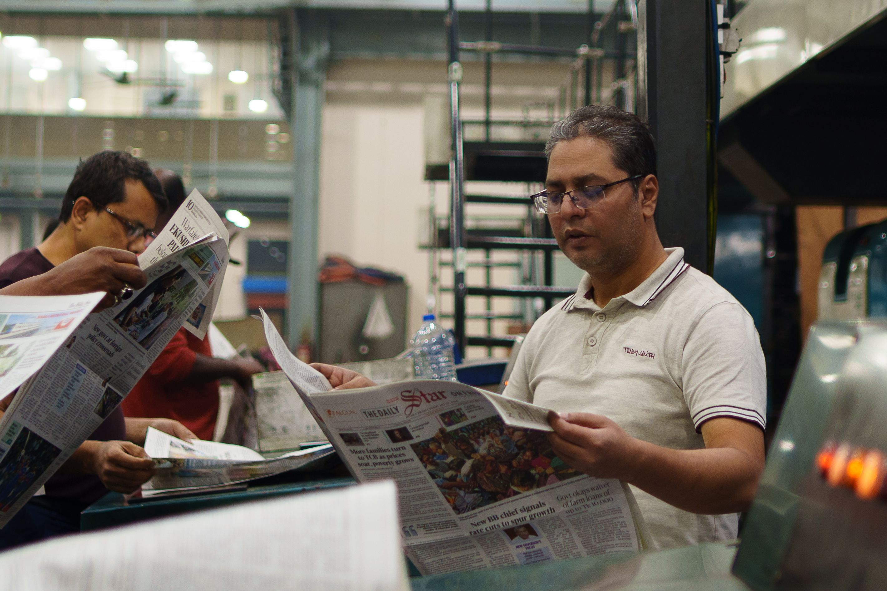 Workers at a newspaper printing press examining freshly printed copies