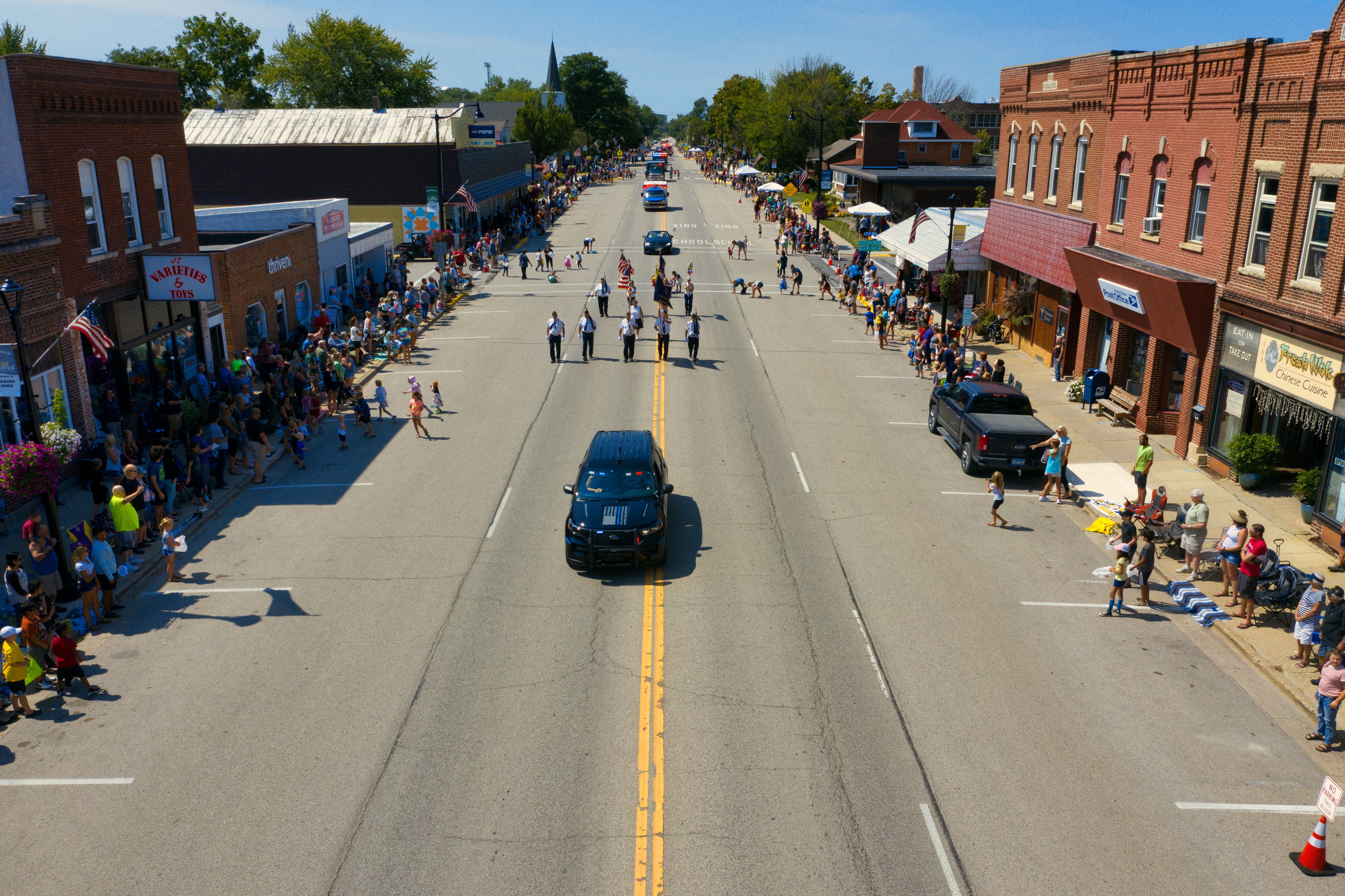 Aerial view of a lively small-town parade with crowds lining the streets